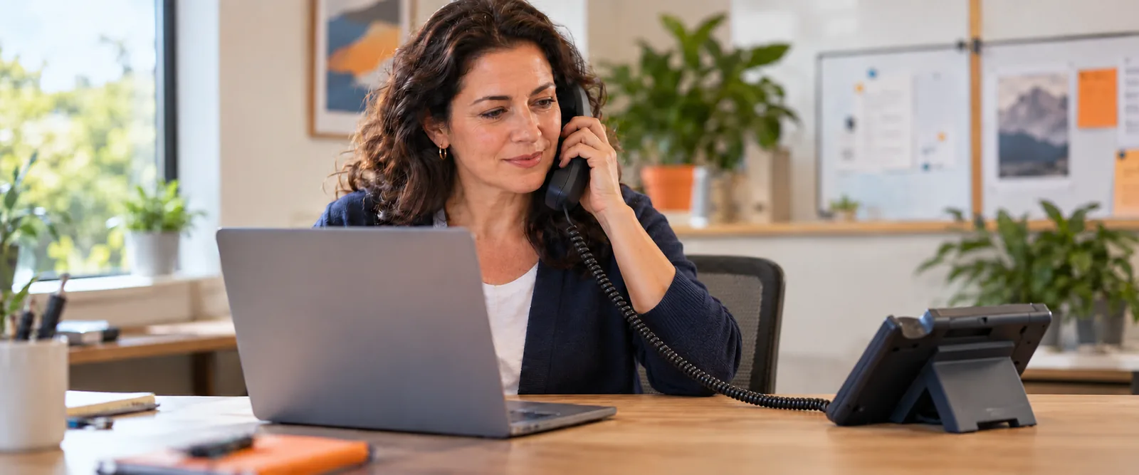 Original editorial illustration of a staff member answering a business desk phone beside a laptop